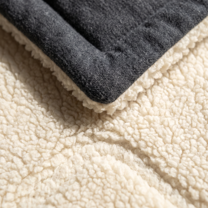 A close photograph of the fabric folded back on itself, the charcoal flannel face above and the deep cream sherpa pile below, each fibre visible in raking light