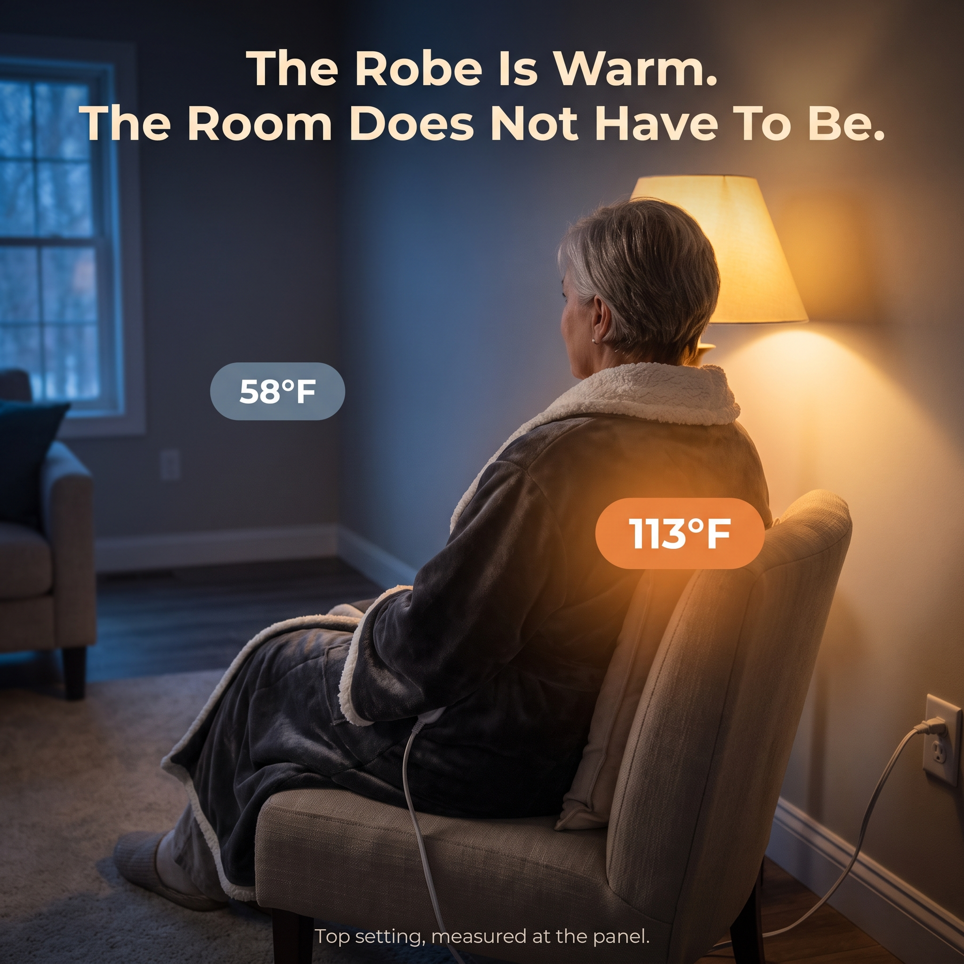 A woman seen from behind sitting in an armchair in a cool blue room wearing the charcoal heated robe, with a warm badge reading one hundred and thirteen degrees Fahrenheit over the panel on her back and a cool badge reading fifty eight degrees Fahrenheit out in the room, under the line The Robe Is Warm, The Room Does Not Have To Be